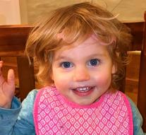A toddler, Leah, smiles and waves at the camera.